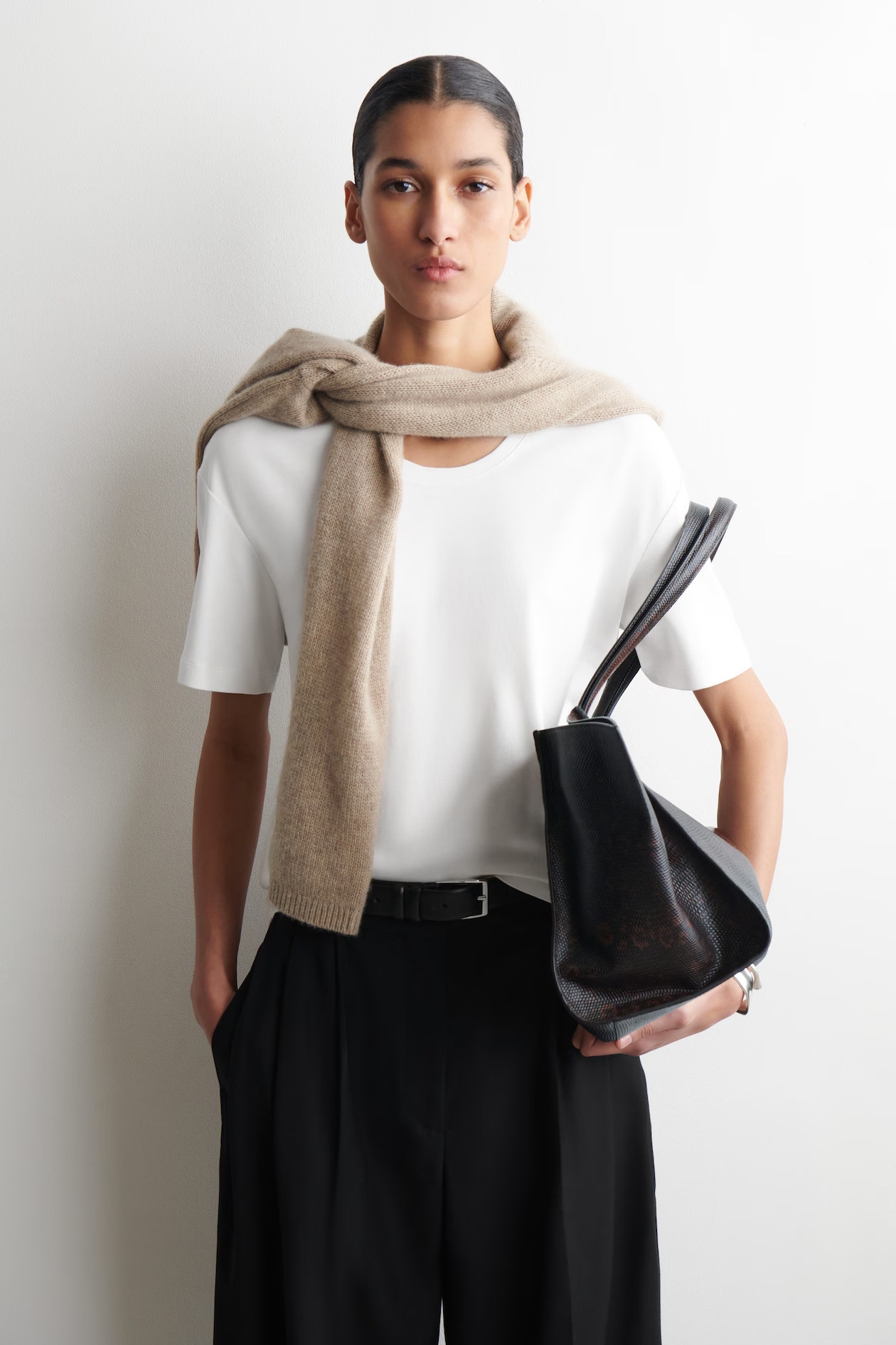 Minimal outfit with white T-shirt, knit over shoulders, black trousers and tote